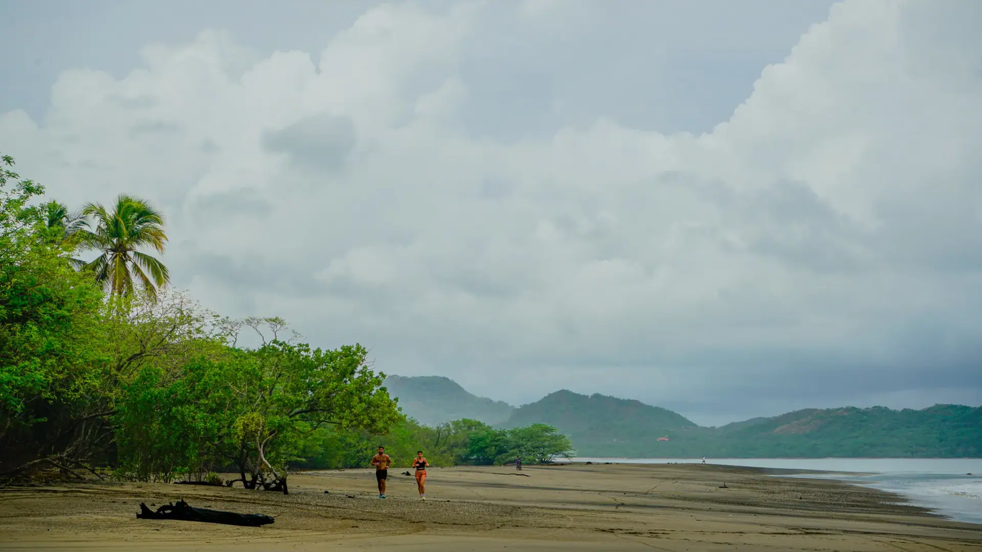 Caminantes en una playa amplia de arena oscura bajo un cielo dramático